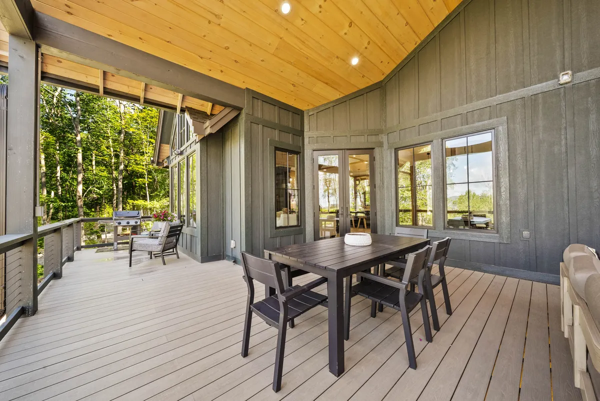 An inviting outdoor dining area is featured, with a sturdy wooden table, a covered wooden ceiling, large windows overlooking greenery, and a sense of privacy. The setting is perfect for sunset dinners, morning coffee, or sharing a glass of wine in a natural setting.