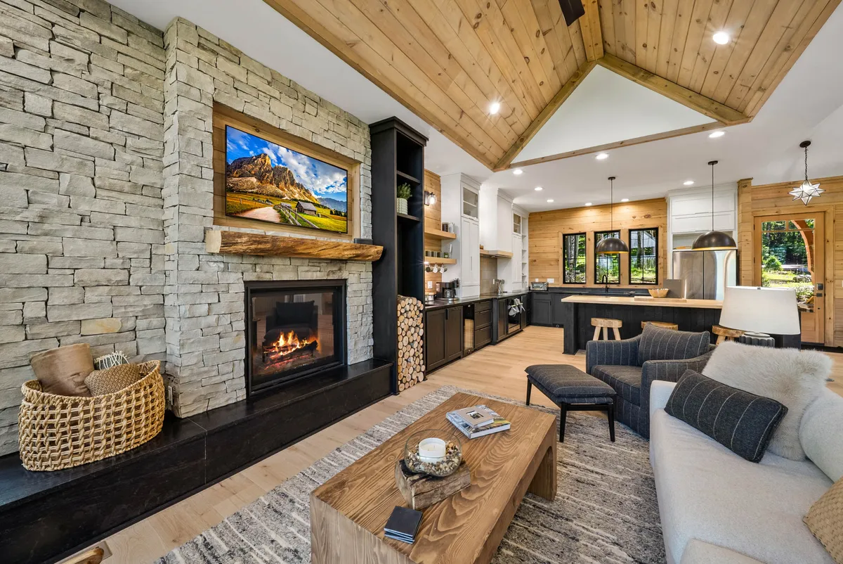 A cozy living space featuring a striking fireplace set against a wooden ceiling, with large windows bringing in natural light. The room is arranged for relaxing and entertaining, with a comfortable sofa and coffee table oriented toward the fire.