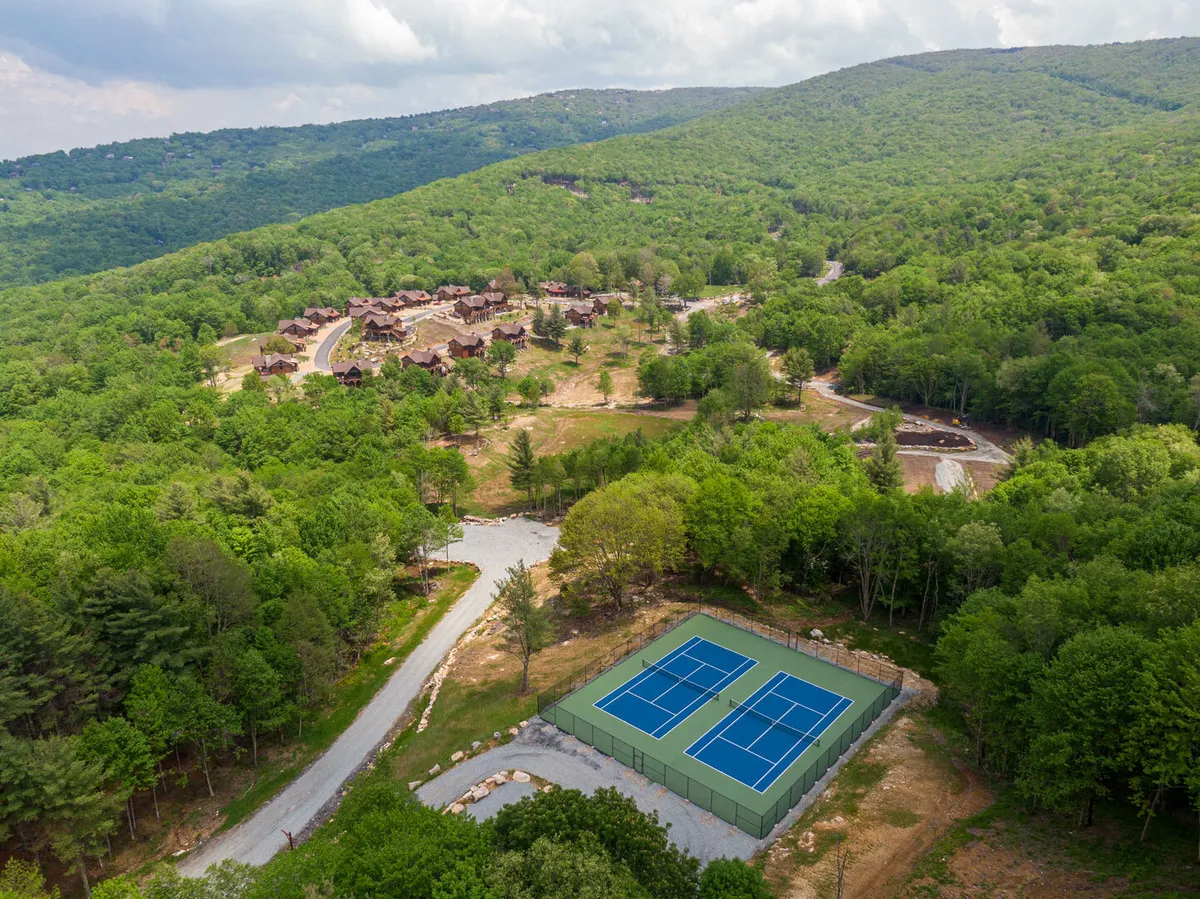 A vibrant view of the community's tennis courts framed by lush greenery and nearby residential buildings. The space is visibly designed for active group play and larger social or sporting events, inviting engagement and friendly competition.