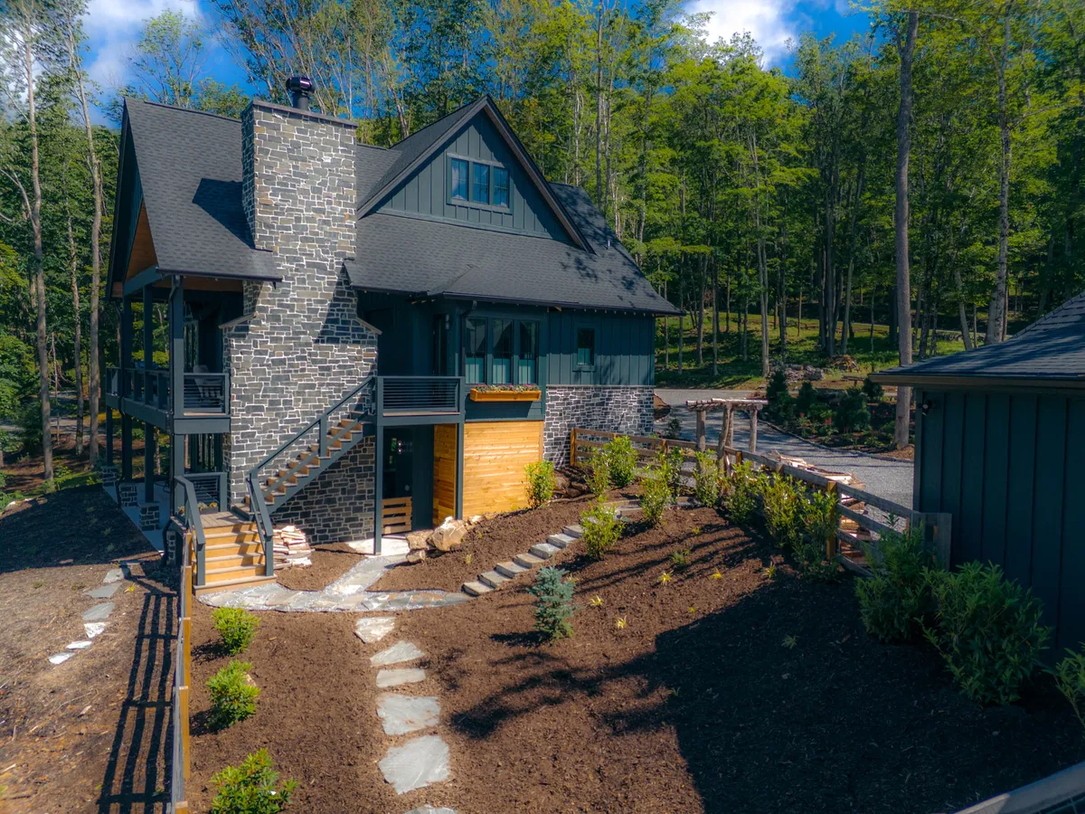This image captures the lodge's beautiful stone chimney, inviting wooden stairs leading to the entrance, manicured garden, and the overall structure of the house. The soft sunset light creates a welcoming, tranquil atmosphere, suggesting peaceful evenings and a connection to nature.