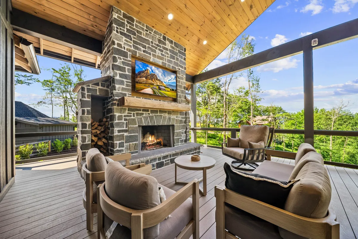 An exterior lounge setting with a stone fireplace, cushioned seating, and a mounted television above the hearth. The area overlooks mountain vistas and is designed for both relaxation and entertaining, especially during sunset or under starry skies.