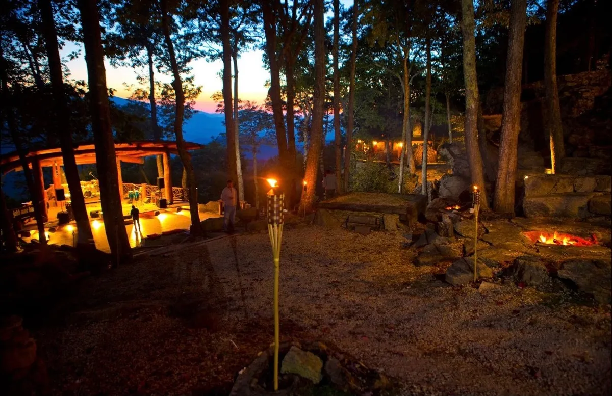 An inviting outdoor seating area featuring a fire pit surrounded by comfortable chairs and tiki torches, set against a wooden structure. The atmosphere is cozy and communal, perfect for relaxing evenings and socializing after a day spent outdoors.