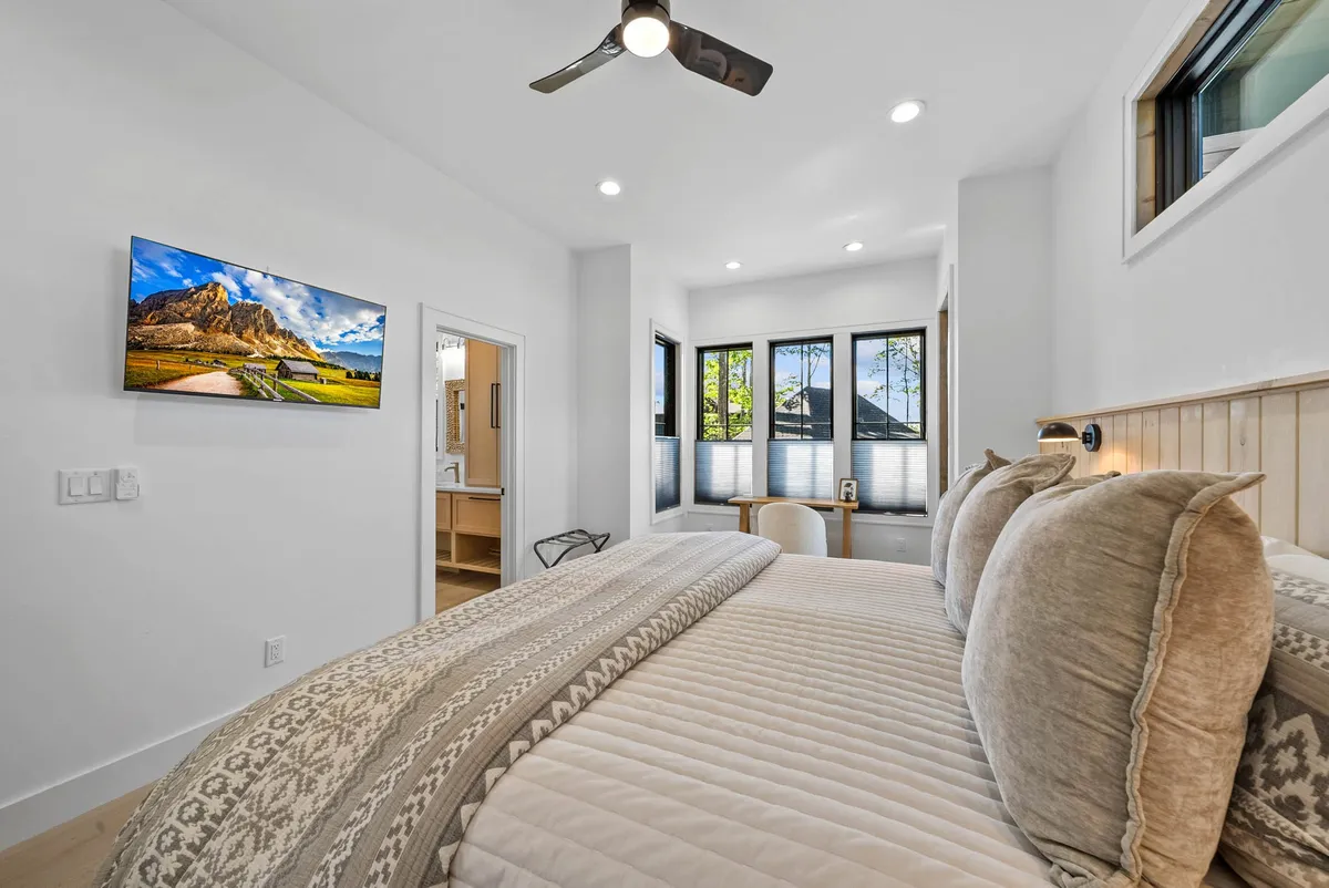 This bedroom features a comfortable bed with decorative pillows, a wall-mounted TV, and large windows letting in natural light. The furnishings are adaptable, emphasizing comfort, privacy, and flexibility for different group needs.