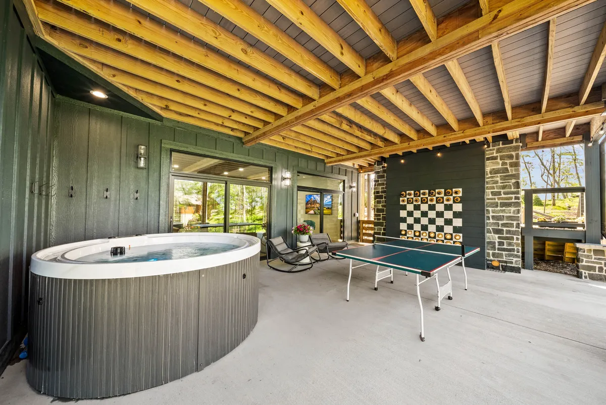 A spacious, light-filled indoor recreation area includes a hot tub, a ping pong table, and large windows showcasing mountain views. The wooden ceiling and open design provide a warm, inviting environment for both relaxation and recreation.