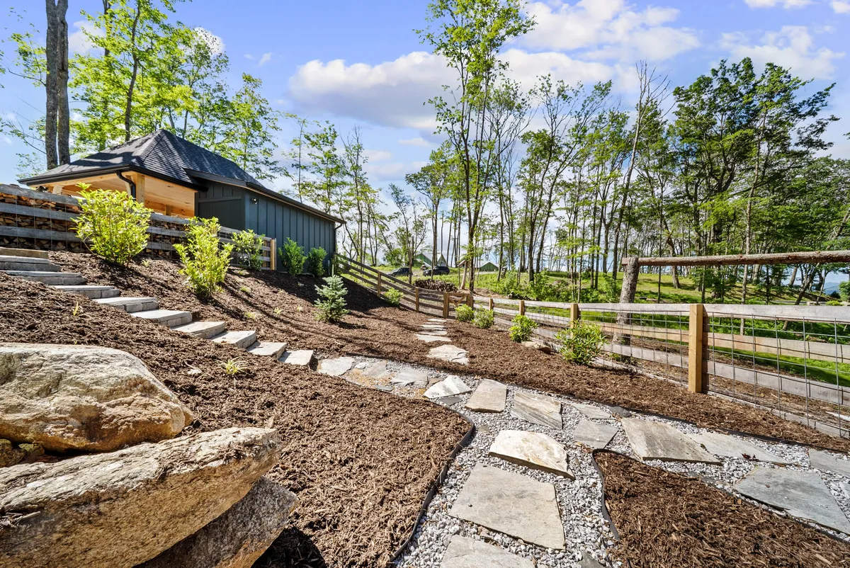 A peaceful exterior scene featuring a fenced yard, stone pathway, and landscaped garden surrounded by mature trees. The fenced area is clearly visible, providing a safe space for children and pets to play while parents relax nearby.