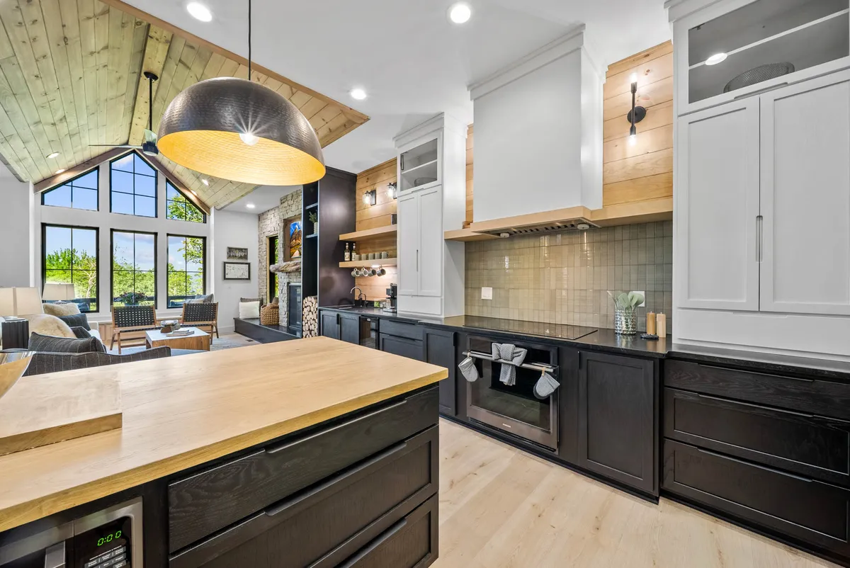 A stylish, modern kitchen with central island, black cabinetry, and wooden ceiling accents. Large windows offer scenic views, and the layout encourages socializing and casual chats around the island.