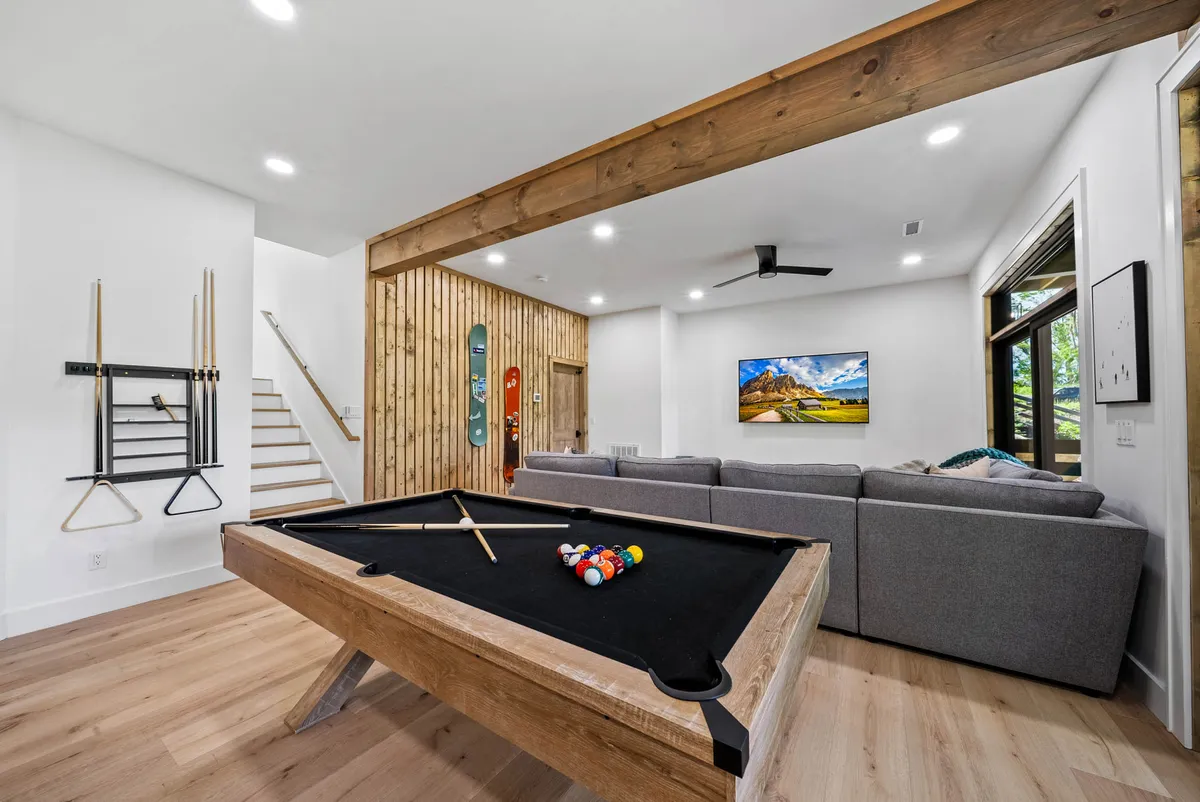 This image shows a vibrant den area featuring a pool table, a cozy sofa, a wood accent wall, and a large TV. The room is designed for fun and relaxation, perfect for game nights or movie marathons, and exudes a warm, playful atmosphere.