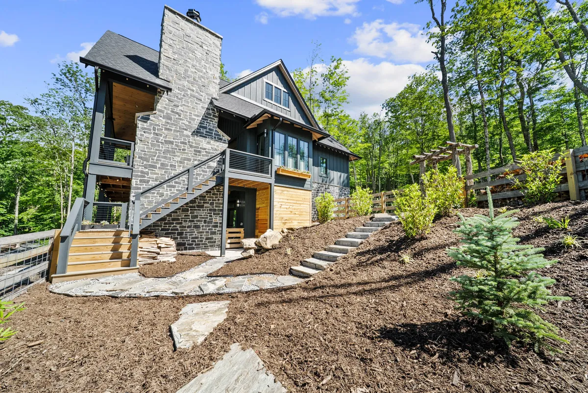 This exterior view highlights a wooden deck and a landscaped garden, bordered by a staircase and stone chimney. The open, green space is inviting, with the deck providing an ideal spot to relax while keeping an eye on pets exploring the garden. The setting conveys a sense of freedom and connection with nature.