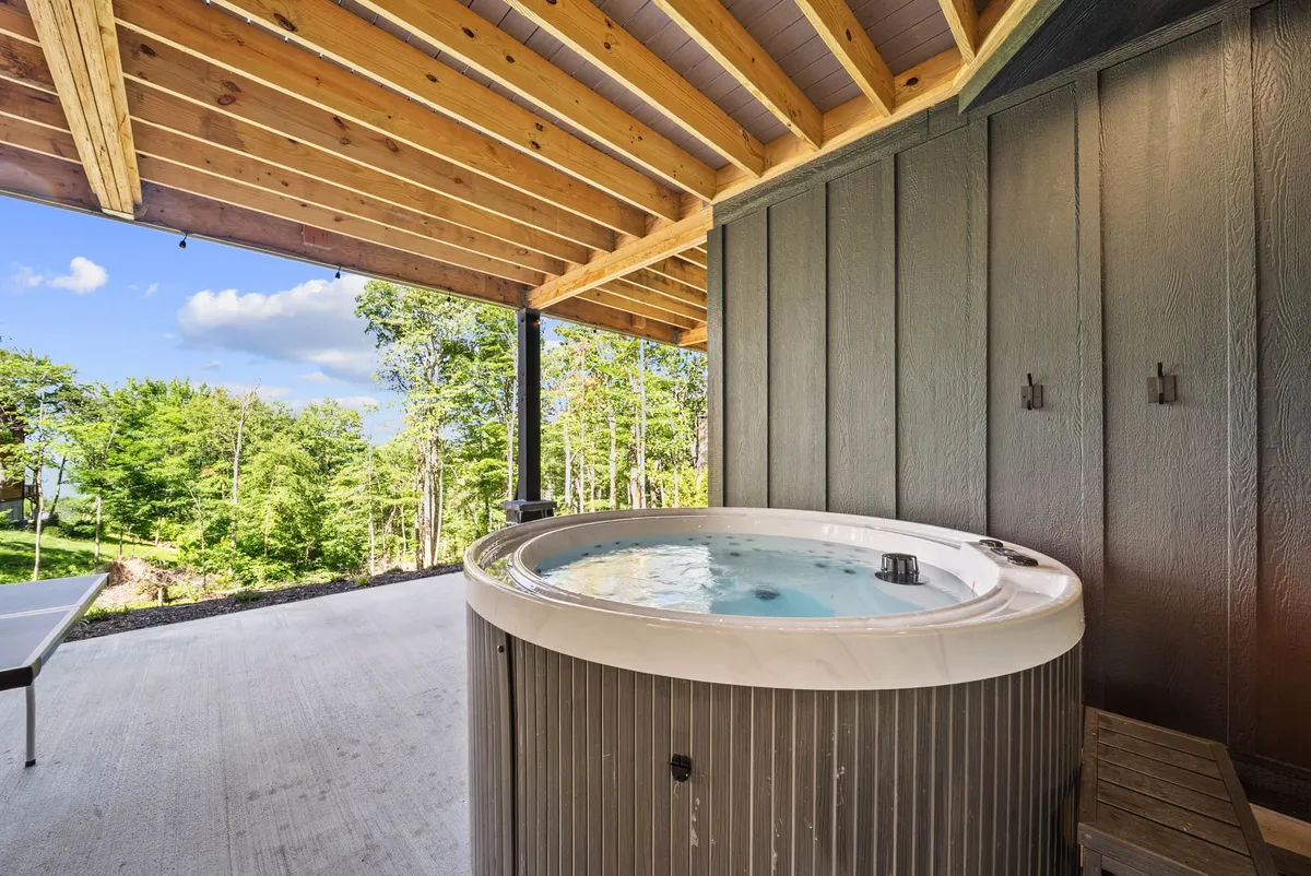 A tranquil hot tub sits beneath wooden beams, surrounded by greenery and natural mountain views. The setup invites relaxation and socializing while connecting guests to the beautiful outdoor environment.